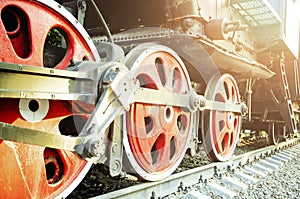 Train drive mechanism and red wheels of an old soviet steam locomotive. Bright rays of the setting sun