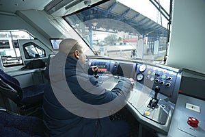 Train driver sitting in the cabin of the passenger train in front of the dashboard
