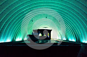 Train driving through a circular green blue tunnel