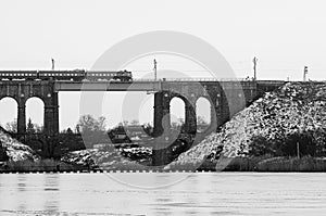Train passing on a high old bridge over the river, winter river in ice and snow. Stone railway bridge with arches