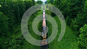 Train on railroad track. forest on both sides. shooting drone