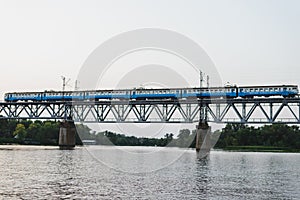 The train is riding over the bridge over the river at sunset