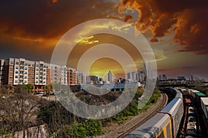 A train riding on the railroad tracks surrounded by lush green trees and skyscrapers and office buildings in the cityscape