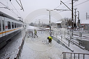 Train station. Speeding train passing by, workers in uniform shovelling snow off a path, Russia, Istra