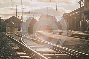 Train station in switzerland, frontal view of the train and train tracks in strong evening sunset light. Typical branch line