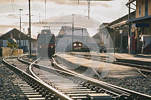 Train station in switzerland, frontal view of the train and train tracks in strong evening sunset light. Typical branch line