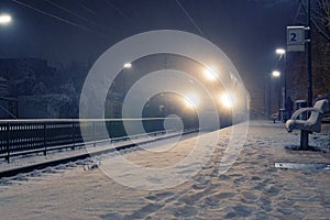 Train with strong headlights arriving at station on a snowy night