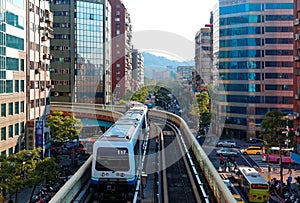 A train of Taipei Metro System traveling on elevated rails of Wenhu Line, entering a station by office towers~ View of MRT railway