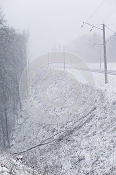 Train tracks in winter, snowing. Slope and fallen tree