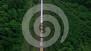 The train transports tanks of crude oil among virgin ecological green forests. Aerial view.