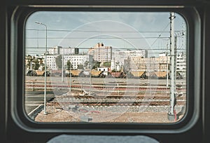 Train window view with old railway, clear blue sky, white and red brick buildings.