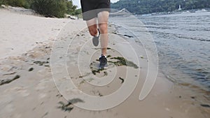 Trained muscular male legs runs on river beach. Front view of active sportive man running near river. Powerful strong legs jogging