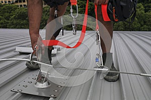 Trained worker clipping stainless industrial locking hook into fall arrest roof anchor point systems