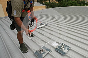 Trained worker clipping stainless industrial locking hook into fall arrest roof anchor point systems