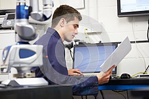 Trainee Engineer Studying Plans With CMM Arm In Foreground photo