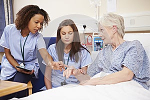 Trainee Nurse Sitting By Female Patient's Bed In Hospital