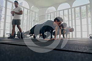 Trainer applauding group of multiracial young adults in sports clothing doing push-ups at the gym