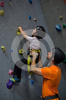 Trainer assisting boy in rock climbing