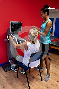 Trainer assisting disabled active senior woman to exercise in exercise equipment