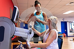 Trainer assisting disabled active senior woman to exercise in exercise equipment