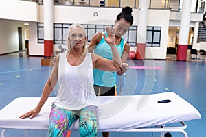 Trainer assisting disabled active senior woman to exercise in sports center