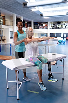 Trainer assisting disabled active senior woman to exercise in sports center