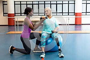 Trainer assisting disabled senior woman to exercise with dumbbell in sports center