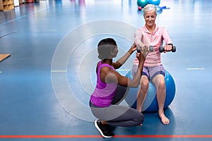 Trainer assisting disabled senior woman to exercise with dumbbell in sports center