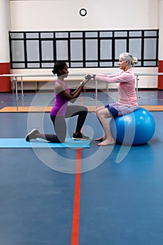 Trainer assisting disabled senior woman to exercise with dumbbell in sports center