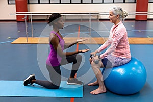 Trainer assisting disabled senior woman to exercise with dumbbell in sports center