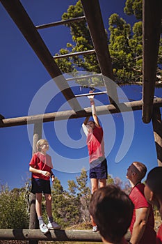 Trainer assisting girl to climb monkey bars during obstacle course training