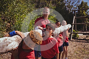 Trainer assisting kids in carrying a heavy wooden log during obstacle course training