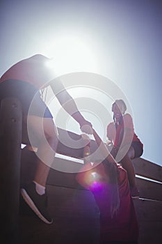 Trainer assisting kids to climb a wooden wall during obstacle course training