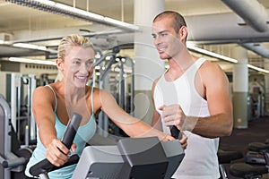 Trainer assisting woman with exercise bike at gym