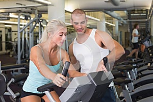 Trainer assisting woman with exercise bike at gym