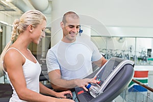 Trainer assisting woman with treadmill screen options at gym