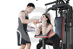 Trainer assisting a young woman on gym equipment