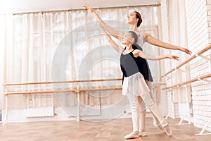 The trainer of the ballet school helps young ballerina perform different choreographic exercises.