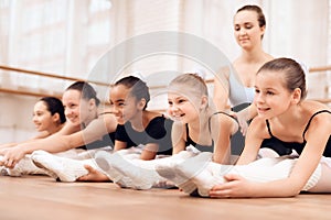 The trainer of the ballet school helps young ballerinas perform different choreographic exercises.