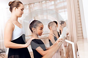 The trainer of the ballet school helps young ballerinas perform different choreographic exercises.