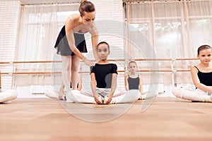 The trainer of the ballet school helps young ballerinas perform different choreographic exercises.