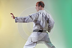 Trainer with black belt doing formal exercises against color background with yellow and green tint