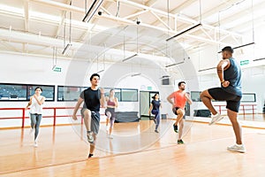 Trainer And Clients Doing High Knee Running While Performing Aerobics