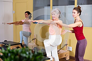 Trainer controlling movements of senior woman doing pilates on combo chair