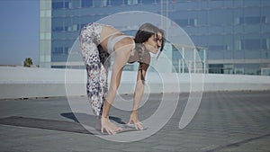 Trainer doing standing forward bend pose on street. Girl stretching body on mat