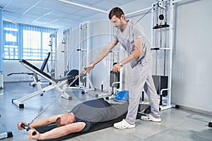 Trainer help young man training on pull cable exercising machine