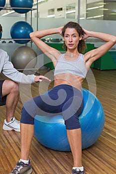 Trainer helping his client doing sit up on exercise ball