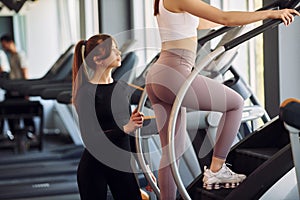 Trainer helping to run the racetrack. Two women in sportive clothes have fitness day in the gym together