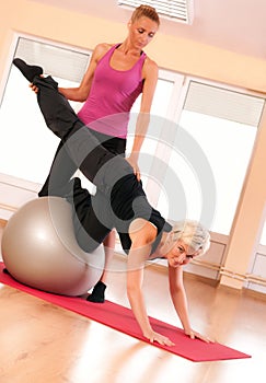 Trainer helping woman in doing exercise on ball