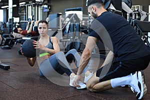 Trainer helping young woman to do abdominal exercises in gym